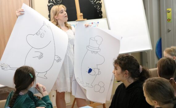 Kobieta trzyma rysunki Muminków, prezentując je z uśmiechem i entuzjazmem.