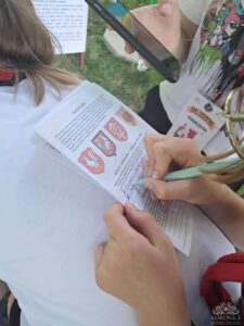 Opis wygenerowany automatycznie: Dziewczynka pisze na kartce, a druga trzyma w ręku telefon komórkowy.