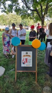 Opis wygenerowany automatycznie: Grupa ludzi stoi wokół znaku, trzymając balony w różnych kolorach, uśmiechając się i rozmawiając.