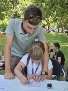 Opis wygenerowany automatycznie: Mężczyzna i mała dziewczynka piszą na papierze, skupieni na wspólnej pracy twórczej.