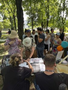 Opis wygenerowany automatycznie: Ludzie przy stole piknikowym podpisują dokumenty.