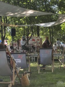 Opis wygenerowany automatycznie: Ludzie siedzą w leżakach w parku, ciesząc się słońcem i relaksując w przyjemnej atmosferze.