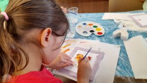 Za stołem przykrytym niebieską ceratą siedzi dziecko, zaangażowane w malowa ine gisowego odlewu.