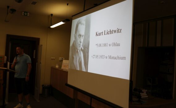 Mężczyzna w jasnoniebieskiej koszulce polo stoi przed ekranem projektora wyświetlającym informacje o Kurtcie Lichtwitzu.