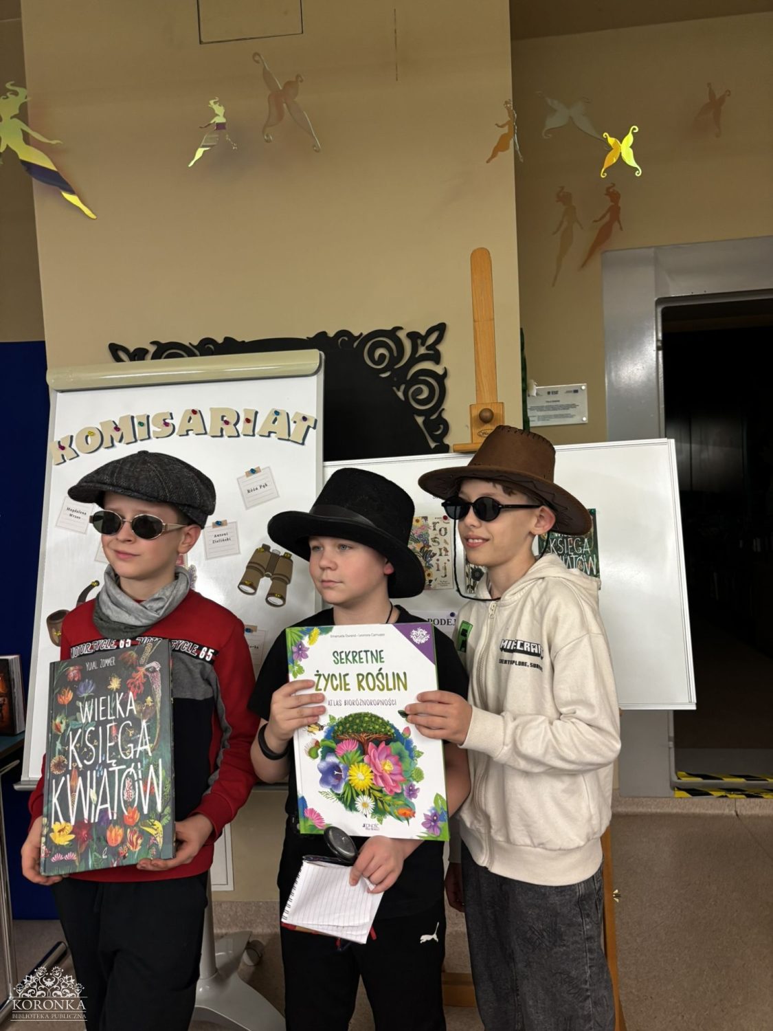 Grupa z dyplomami Opis wygenerowany automatycznie: Trzech chłopców w przebraniach detektywistycznych (kaszkiet, biały kapelusz, okulary przeciwsłoneczne) pozuje wspólnie, prezentując otrzymane dyplomy i nagrody.